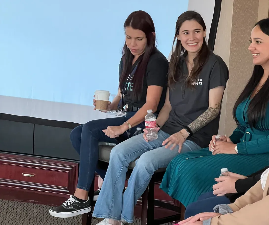 Three women seated at the front of a meeting room, one in a BetterWho shirt